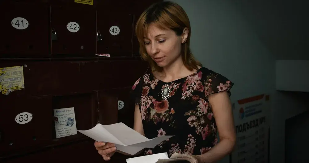 Mulher lendo correspondência em frente às caixas de correio de um prédio