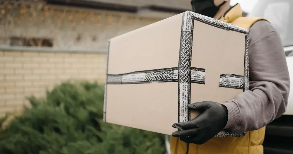 Entregador segurando caixa de papelão em frente a uma casa