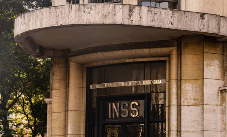 A imagem mostra a fachada de um edifício que abriga o INSS (Instituto Nacional do Seguro Social). A entrada é marcada por uma porta de ferro com a sigla