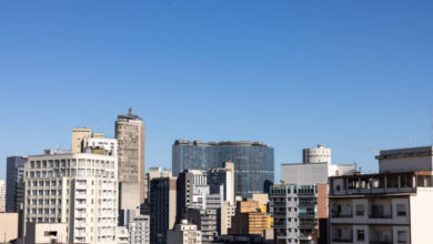 A imagem mostra uma vista panorâmica de um centro urbano, com diversos edifícios de diferentes tamanhos e estilos arquitetônicos. O céu está limpo e azul, e os prédios variam entre estruturas modernas e mais antigas, refletindo a diversidade arquitetônica da cidade.