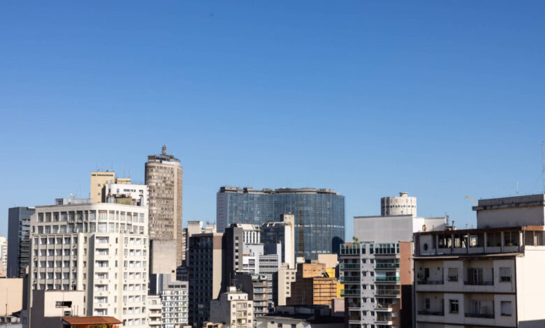 A imagem mostra uma vista panorâmica de um centro urbano, com diversos edifícios de diferentes tamanhos e estilos arquitetônicos. O céu está limpo e azul, e os prédios variam entre estruturas modernas e mais antigas, refletindo a diversidade arquitetônica da cidade.