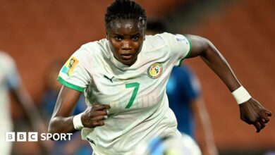 Mama Diop, wearing a white Senegal shirt, chases after the ball