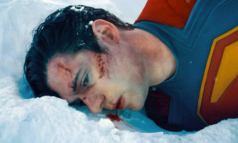 A imagem mostra um homem deitado na neve, vestindo um traje de super-herói com o símbolo de um