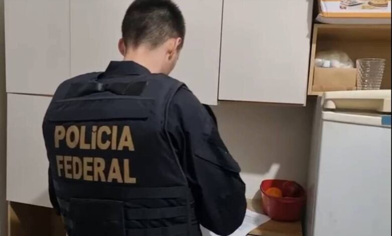 Um agente da Polícia Federal está de costas, usando um colete preto com a inscrição